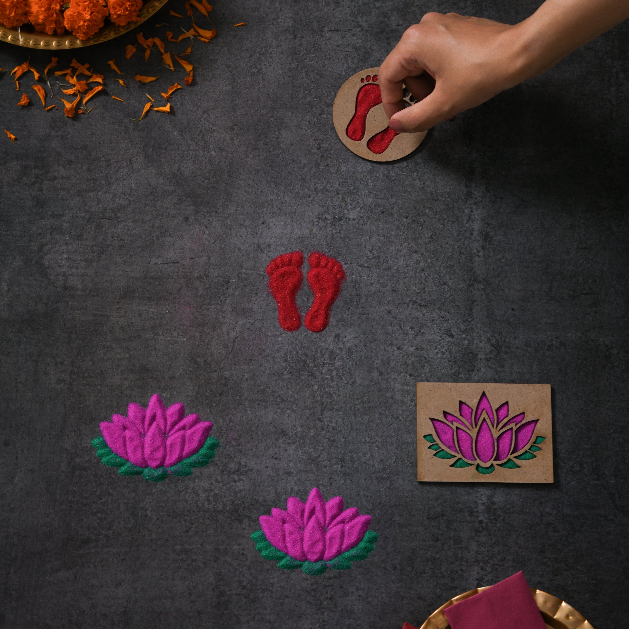 Handmade shapes like red footprints and pink lotus flowers on a dark surface.