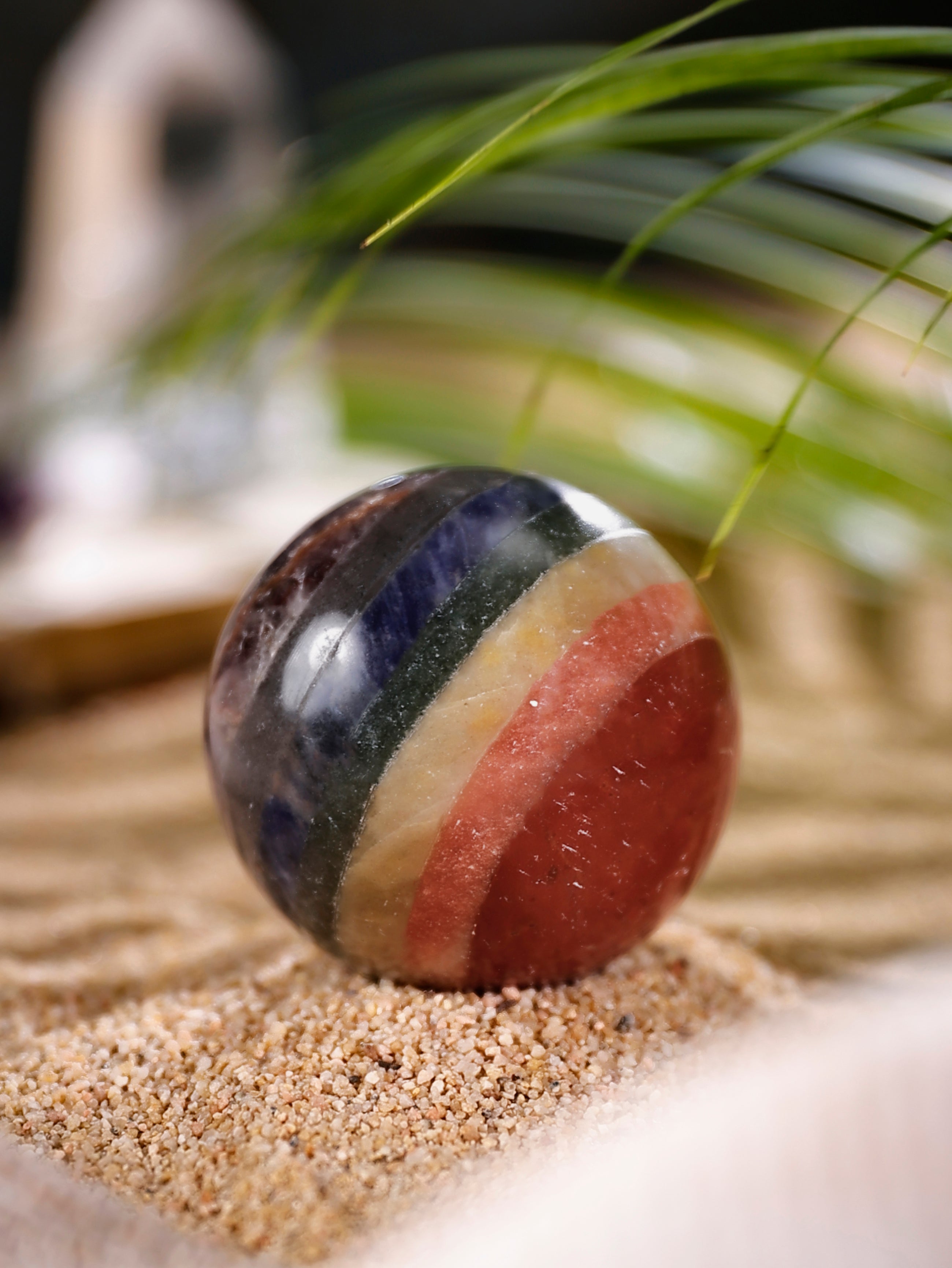 Multicolored spherical object on a sandy surface with blurred greenery in the background