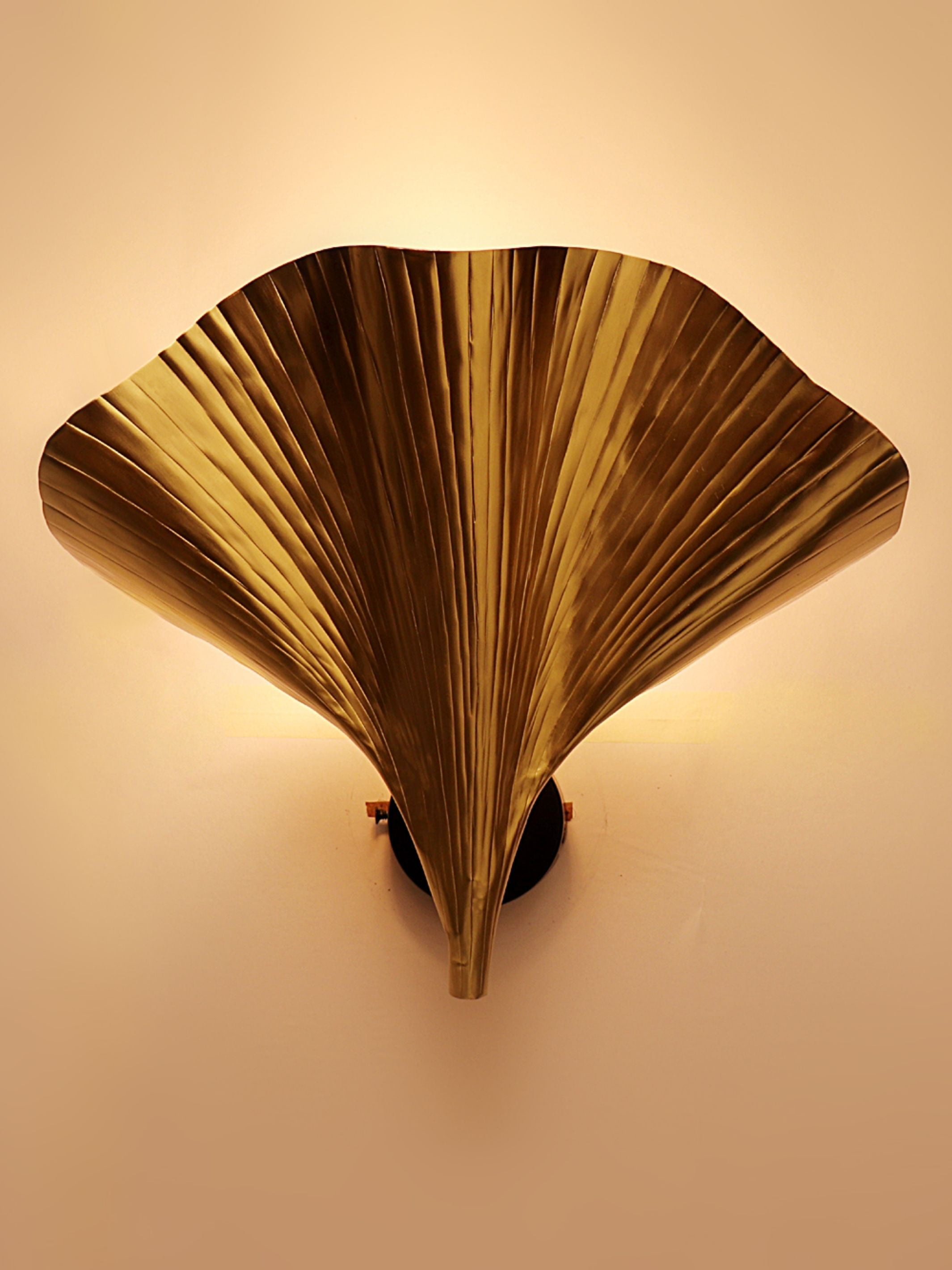 Decorative wall light fixture with fan-like design on a beige wall.