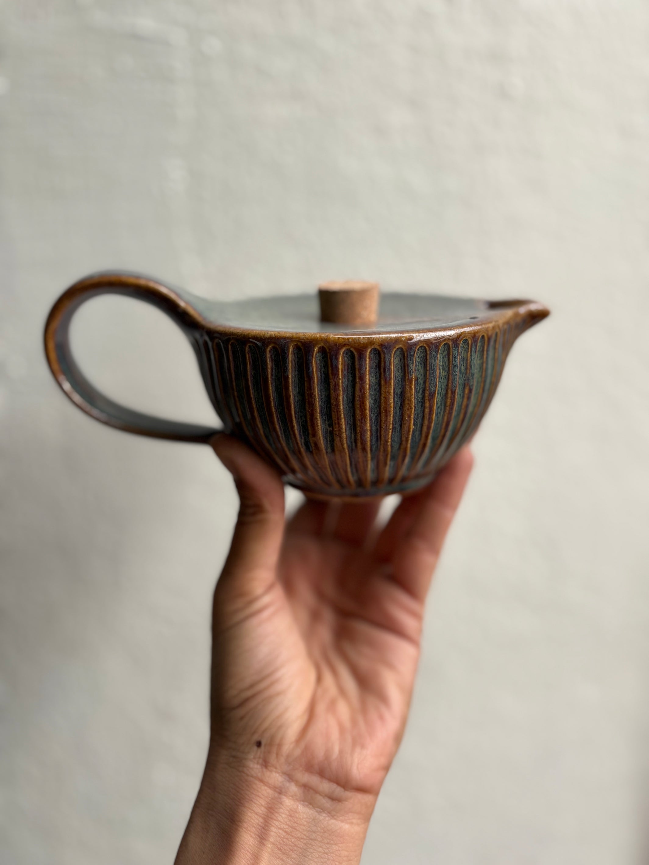 Hand holding a ceramic teapot with a textured surface against a plain background