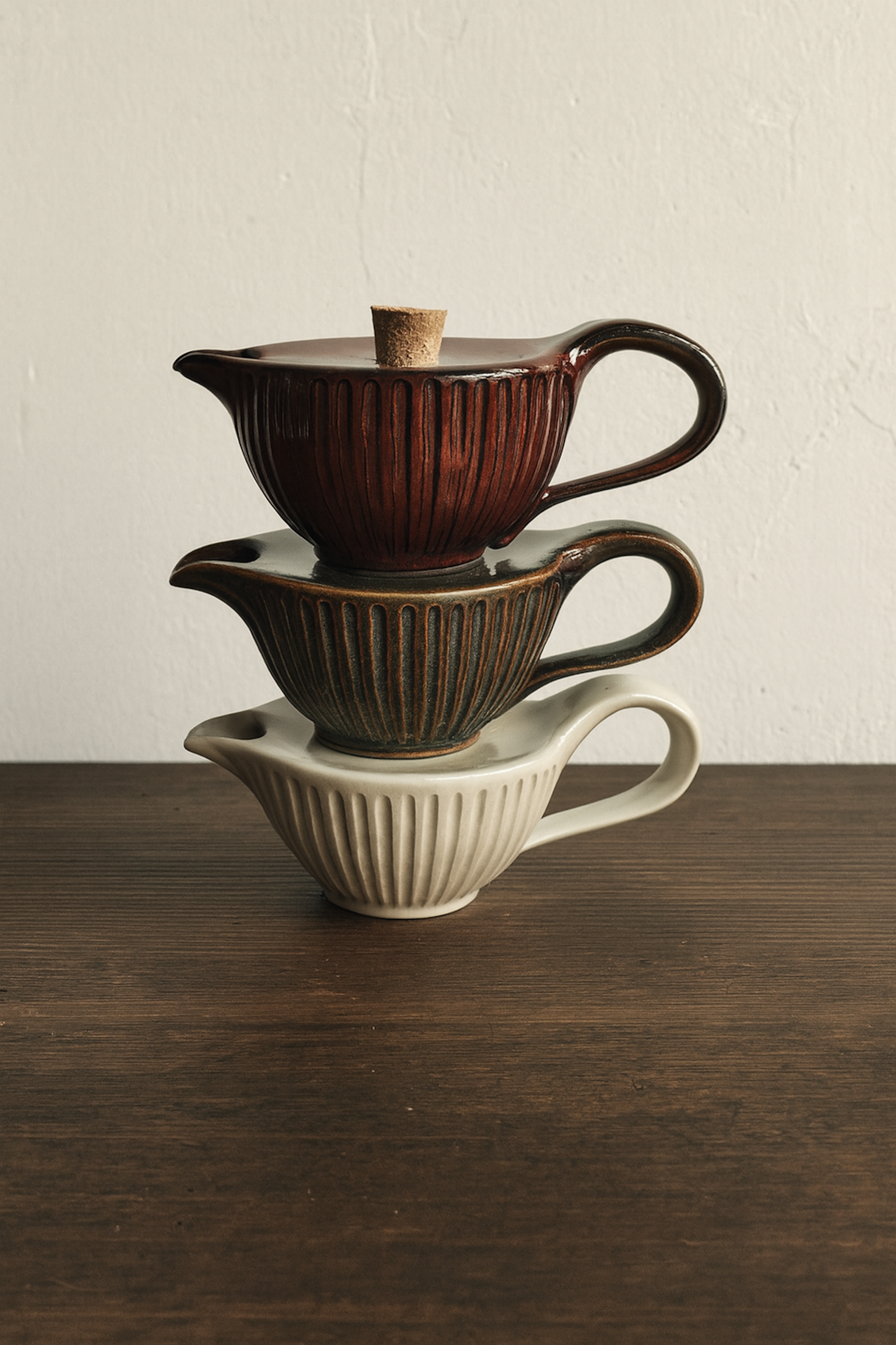 Three stacked ceramic teapots on a wooden surface with a neutral background