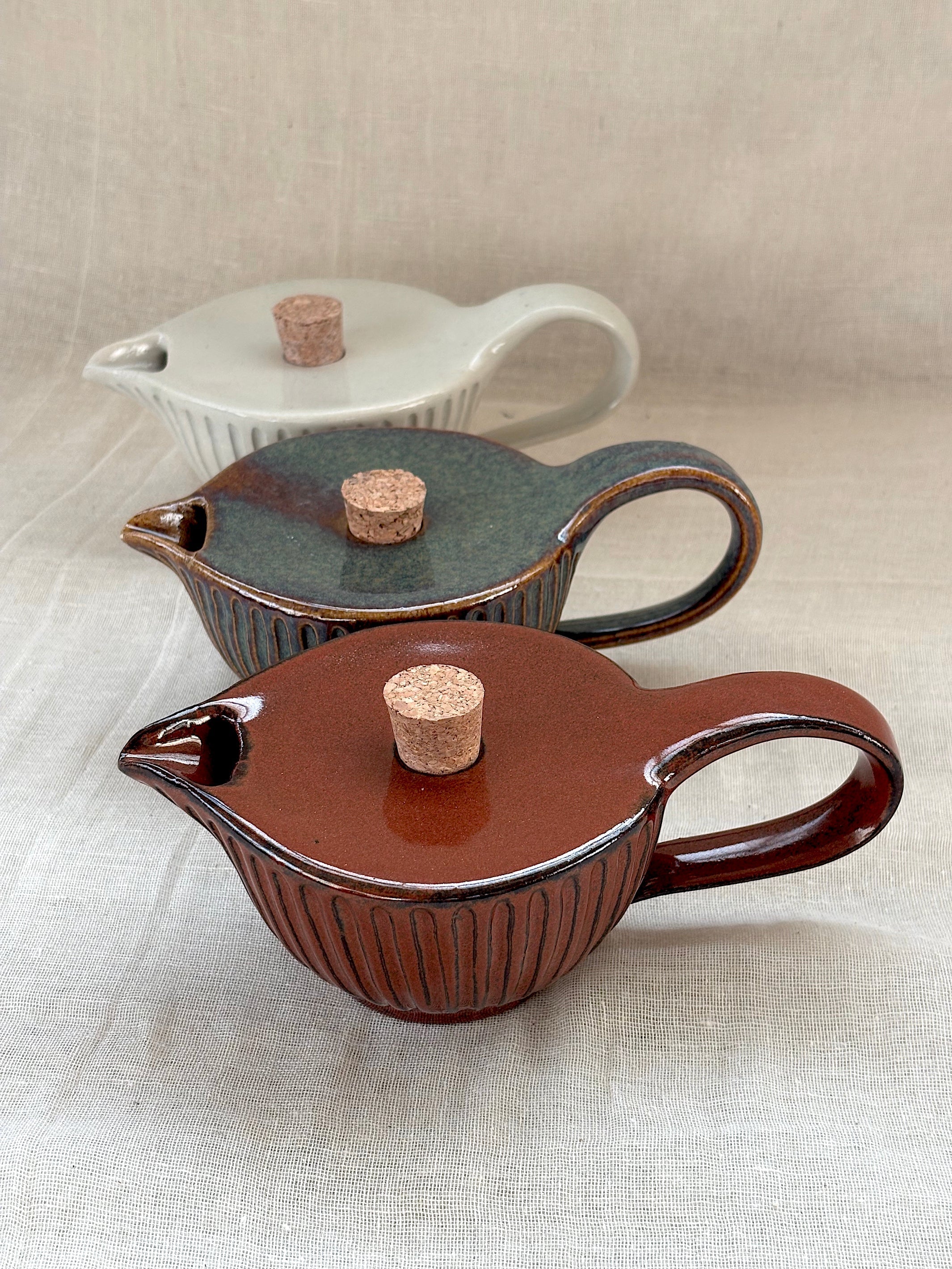 Three ceramic pitchers with cork stoppers on a light fabric background