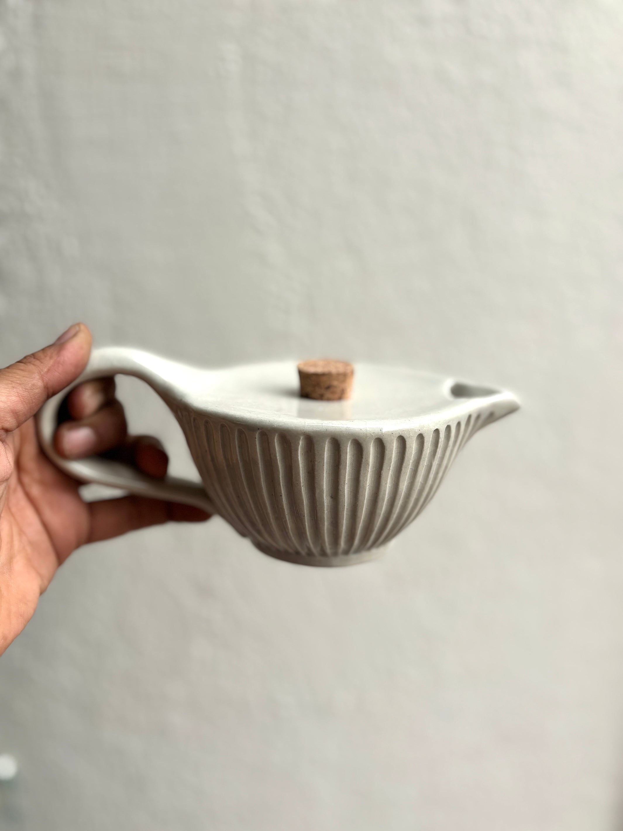 Ceramic teapot held by a hand against a plain background