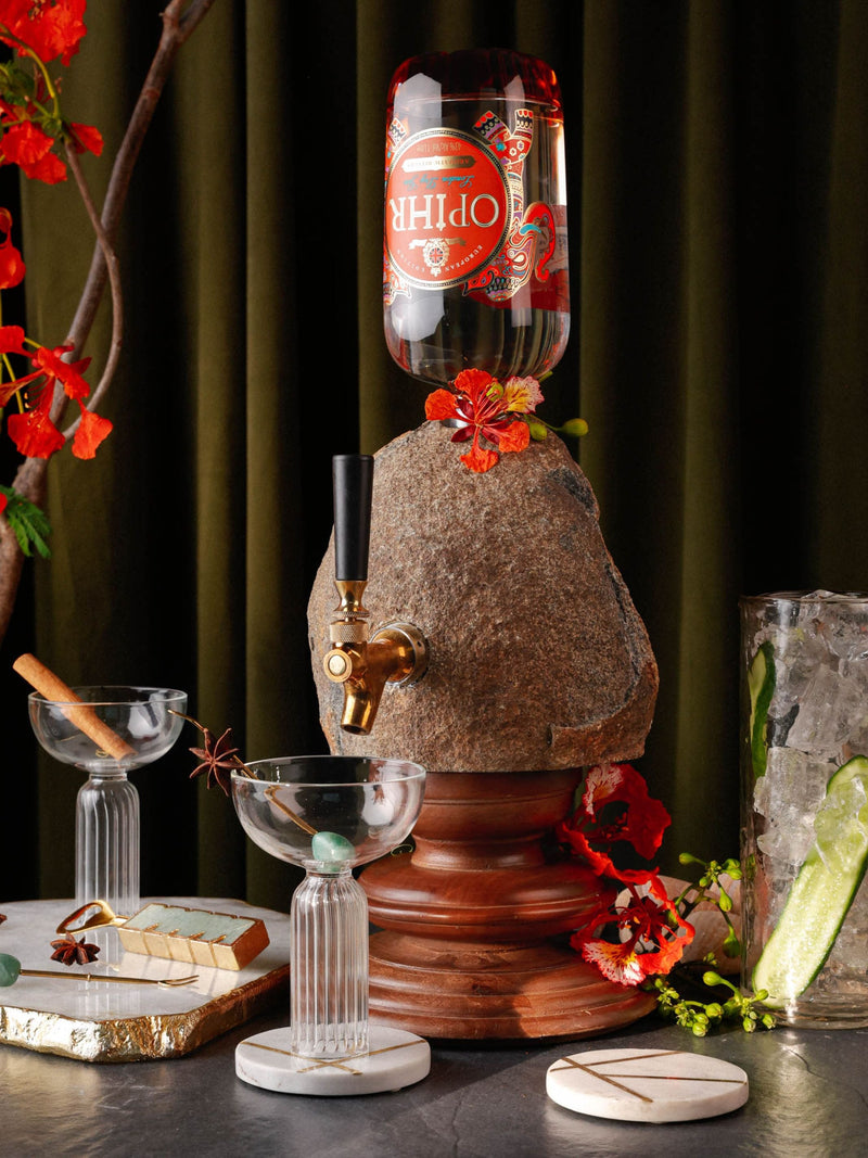 A rustic boulder drink dispenser with brass hardware tap, surrounded by decorative items and a bottle of liquid.