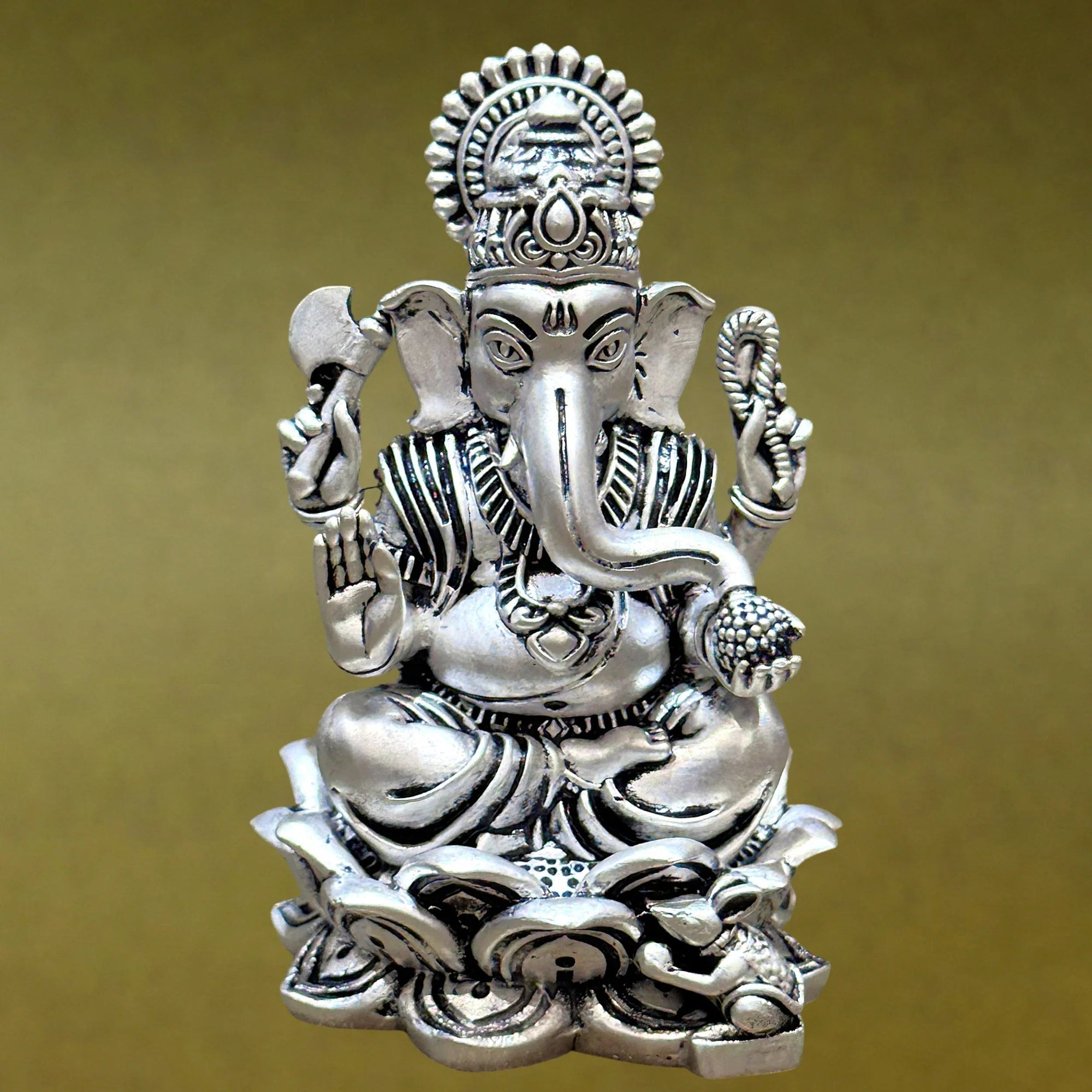 Silver Ganesh idol with detailed carvings on a lotus base against a gold background, Sabera