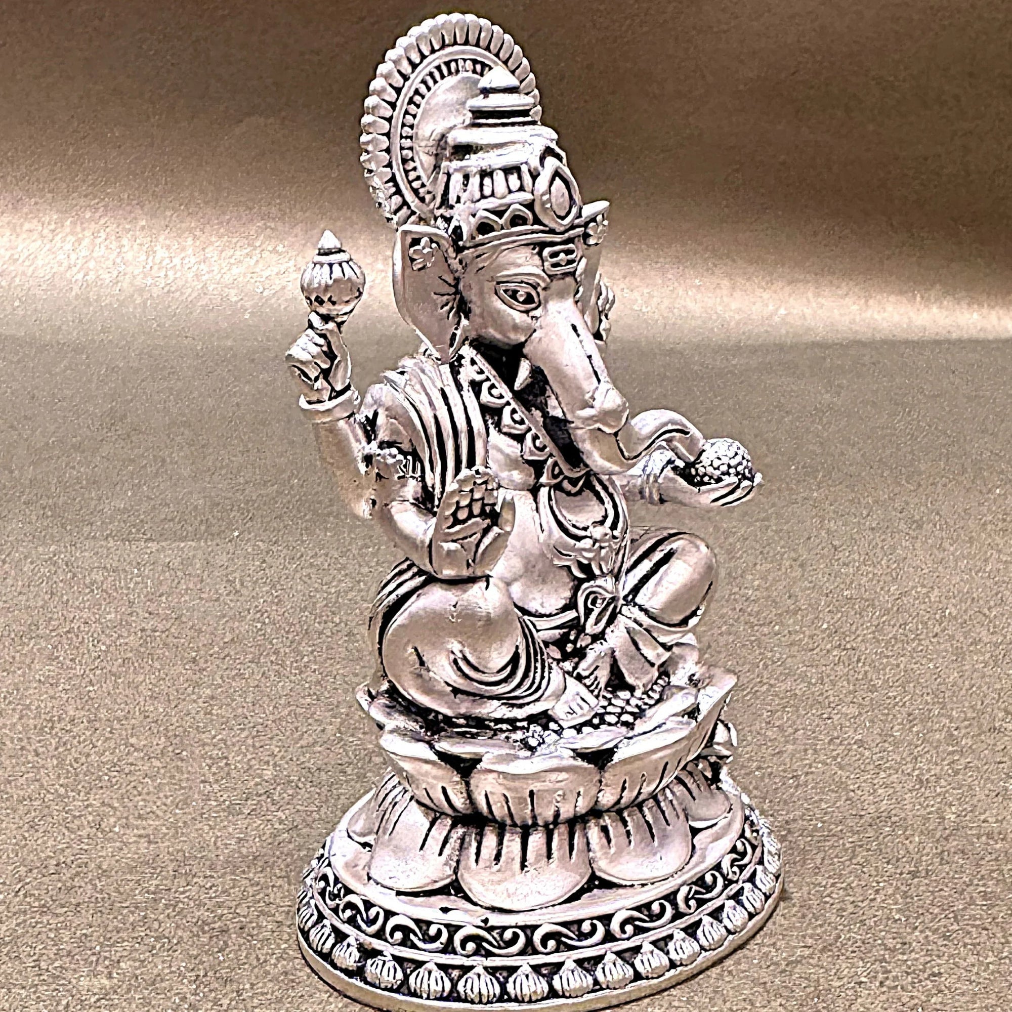 Silver Ganesh statue with intricate detailing on a gold surface, Sabera home decor