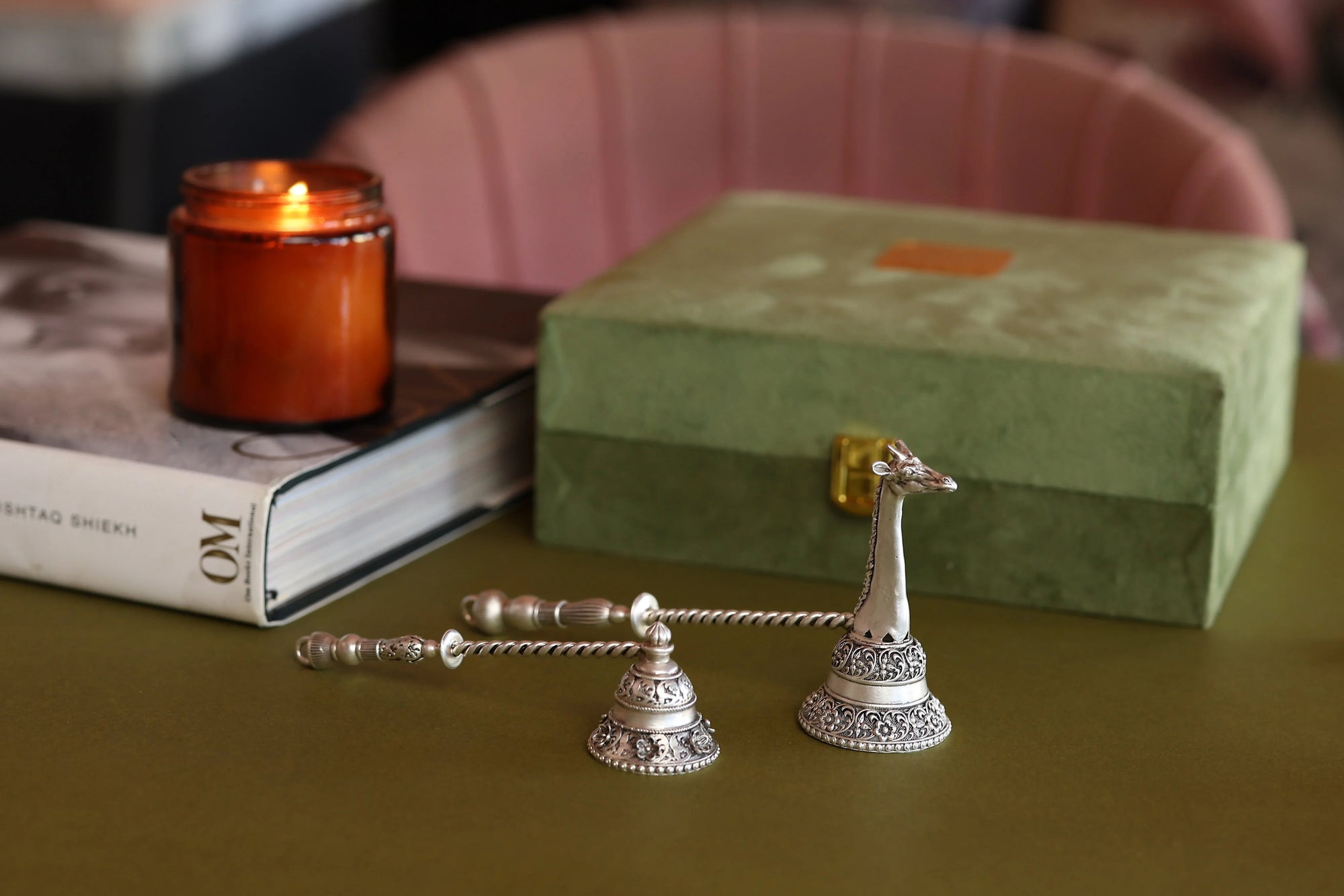 Decorative silver giraffe candle snuffer on table with green box, book, and lit amber candle