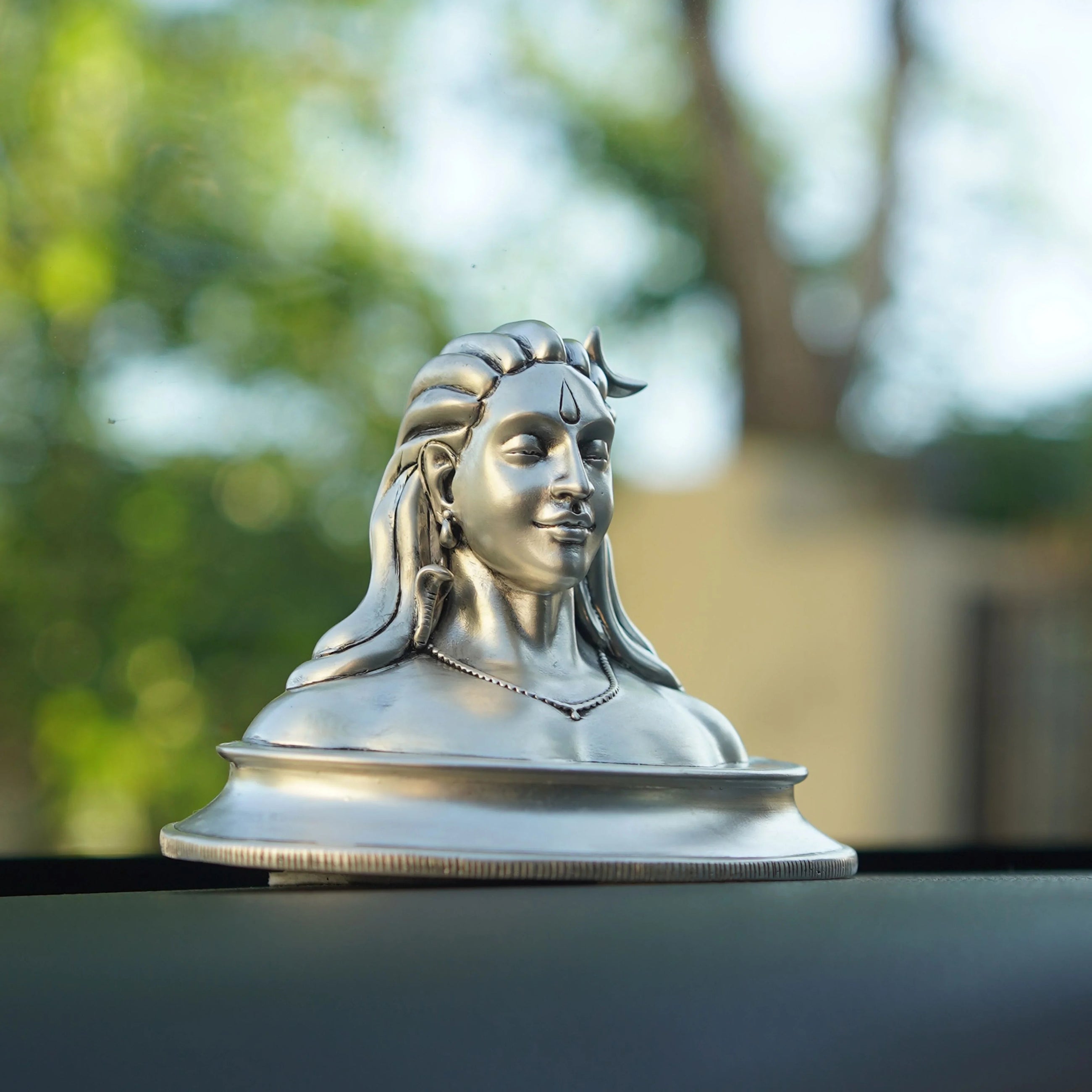 Silver Adiyogi Shiva idol for car dashboard with Sabera branding, outdoor background