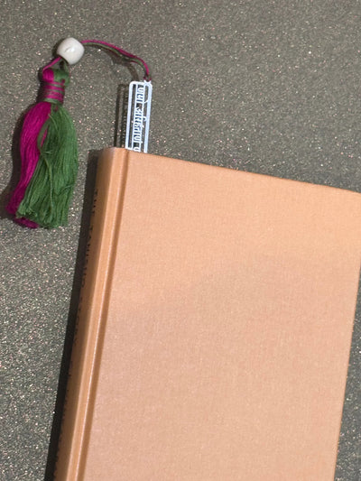 Pink hardcover book with handmade pink and green tassel bookmark on glitter surface