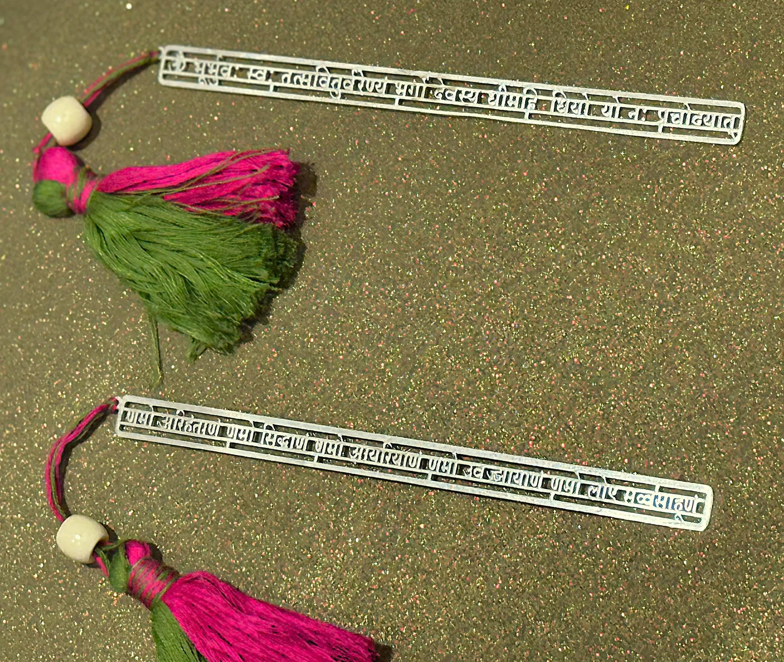 Decorative metal bookmarks with pink and green tassels on a glittery gold background, Sabera