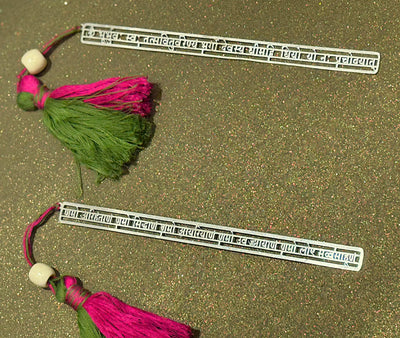 Decorative metal bookmarks with pink and green tassels on a glittery gold background, Sabera