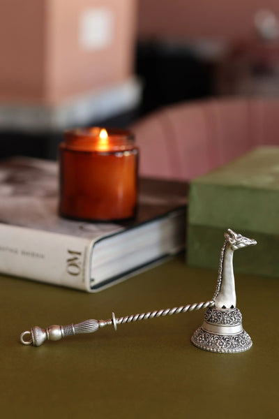 Vintage silver giraffe candle snuffer with ornate handle on table, candle in background