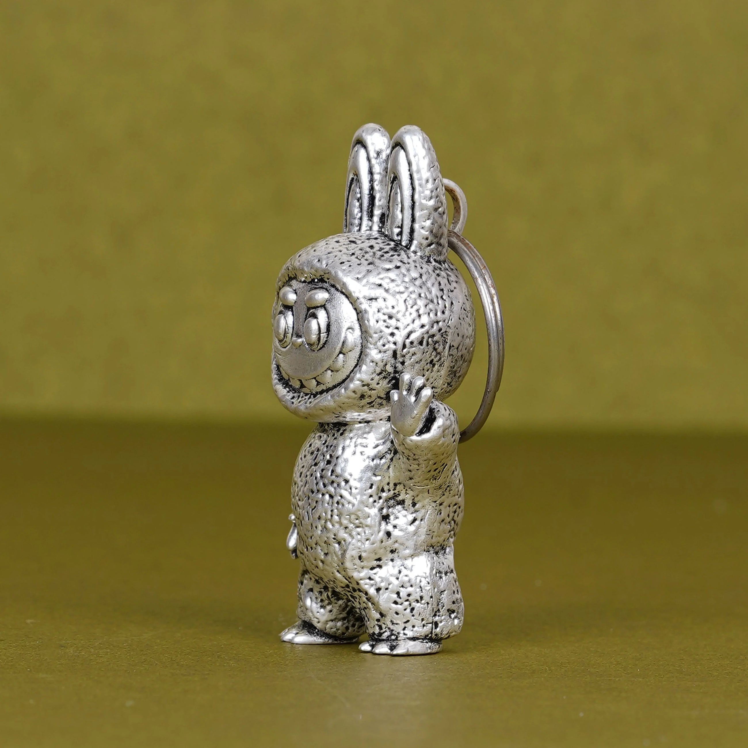 Elegant Labubu silver plated 3D keychain on olive green background, Sabera product