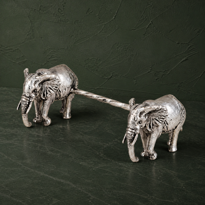 Two silver-plated elephant spoon rests on a dark green studio surface