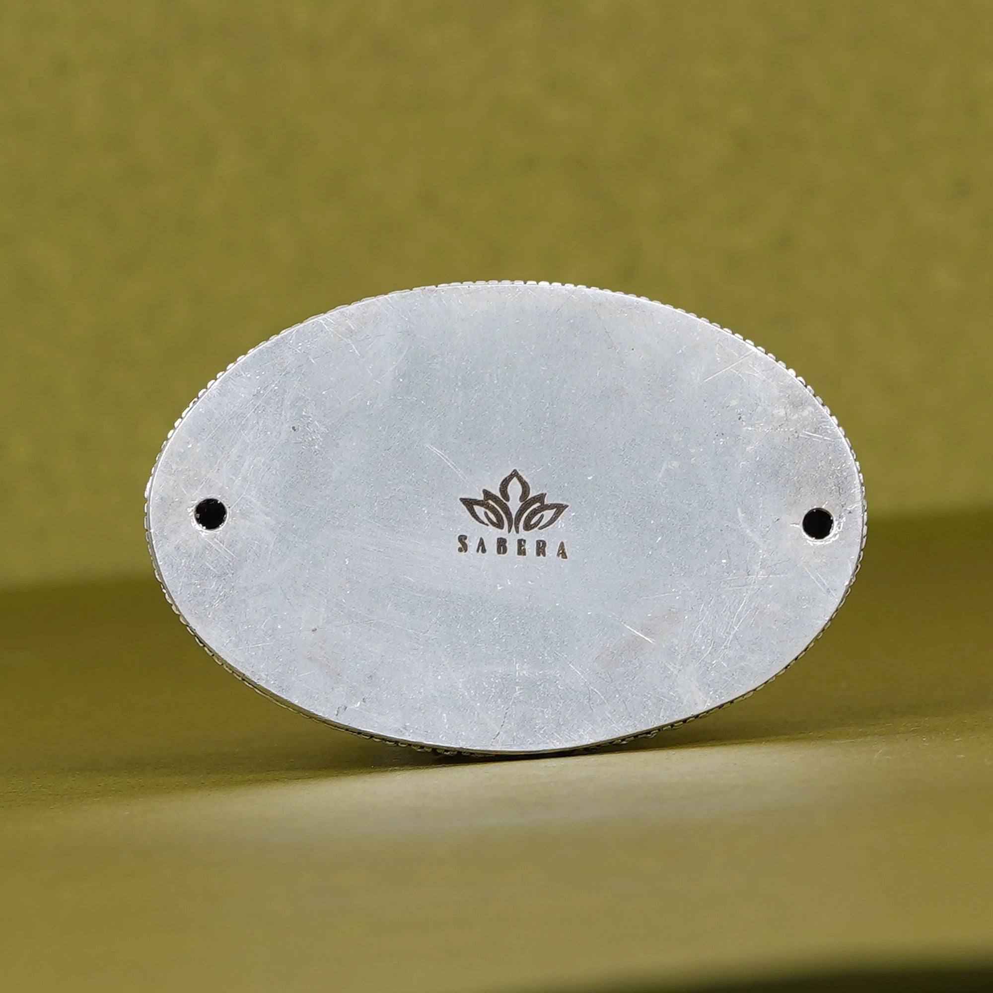 Bottom view of oval metal base with Sabera logo, green background, Hanuman idol accessory.