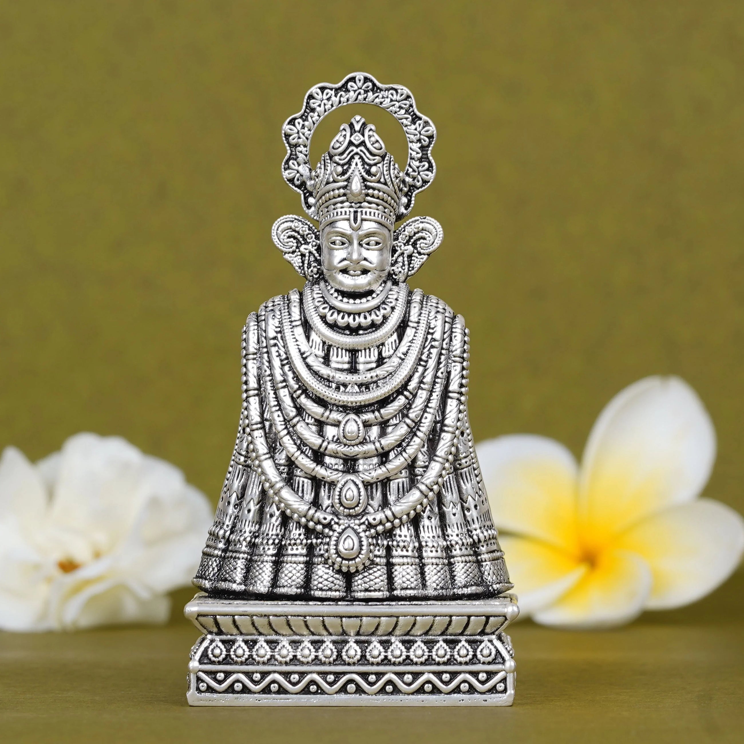 Silver Khatu Shyam Ji idol for car dashboard with detailed ornaments, flowers in background