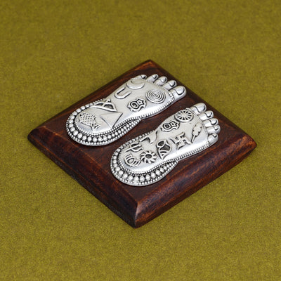 Lakshmi Charan foot silver charm on square wooden base, angled view