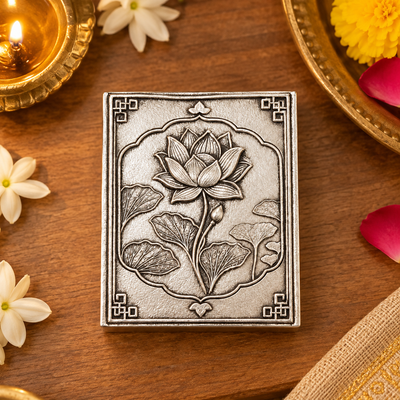 Lotus matchbox cover beside a lit brass diya and flowers in a pooja setting