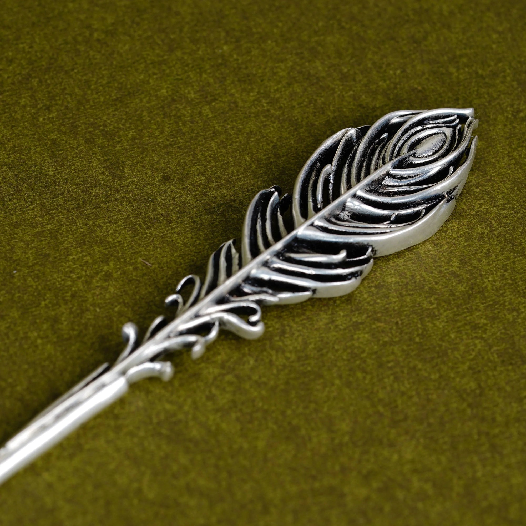 Silver Mor Pankh Tilak stick with peacock feather design on olive green background