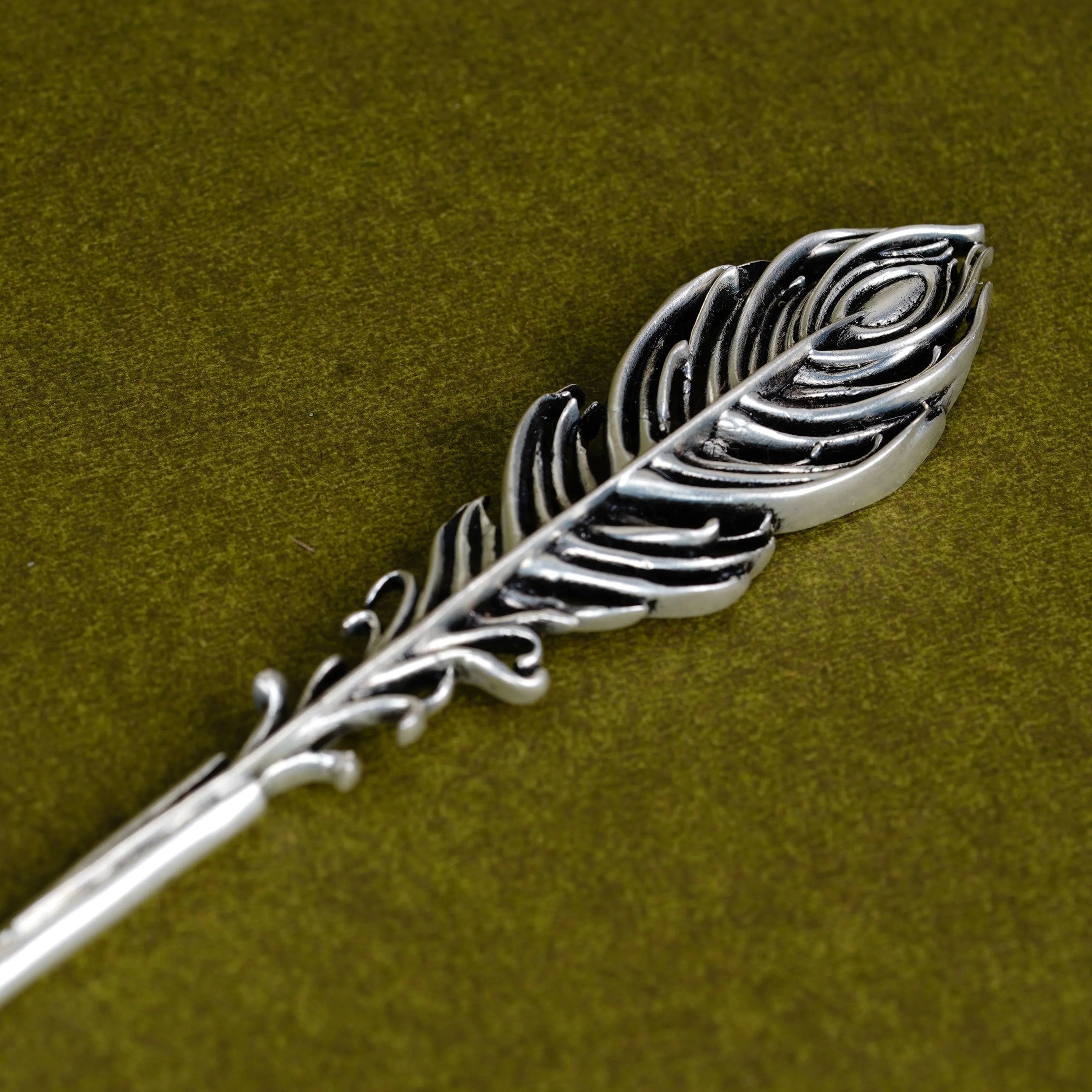 Silver Mor Pankh Tilak stick with peacock feather design on olive green background