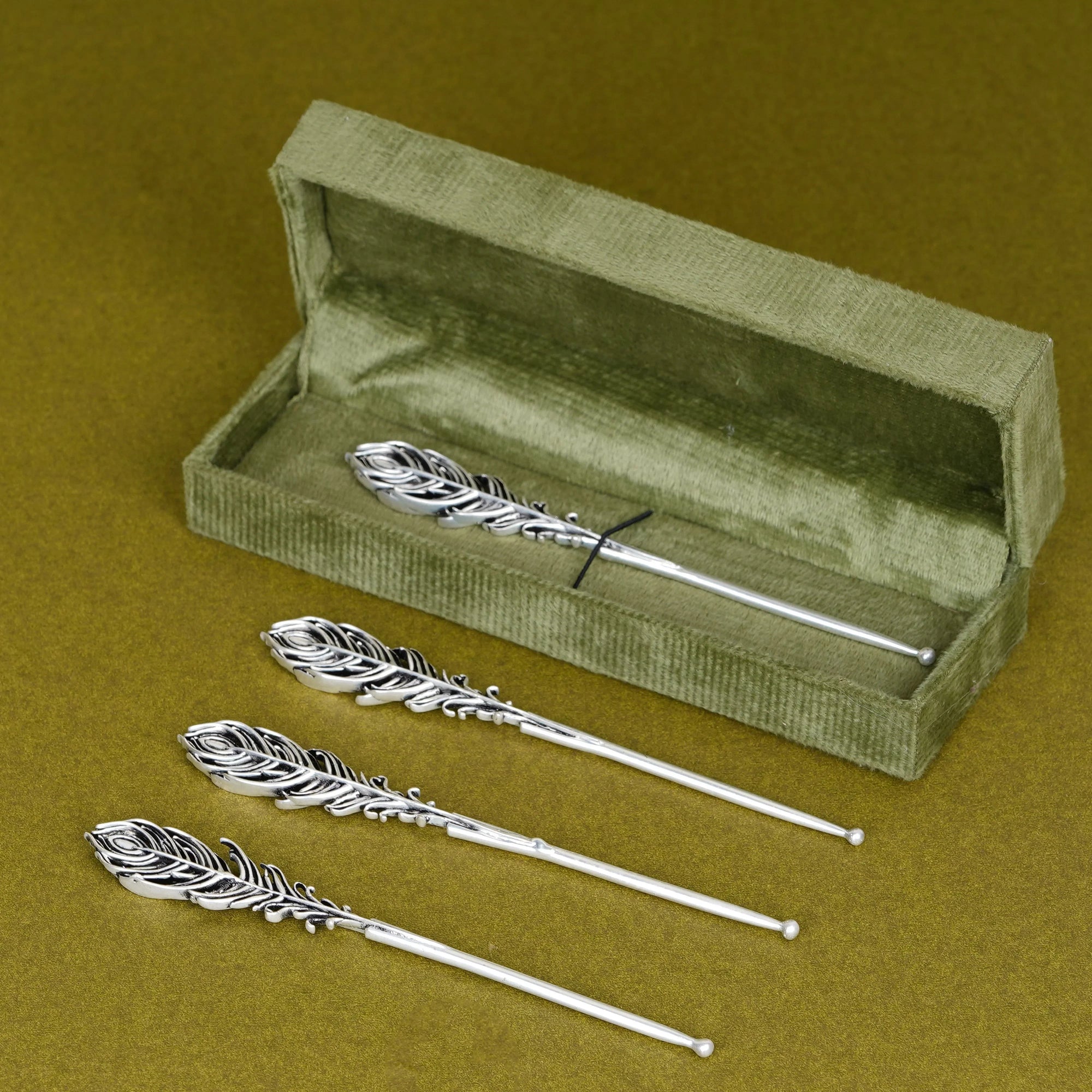 Silver peacock feather tilak sticks with green velvet box on mustard background, Sabera