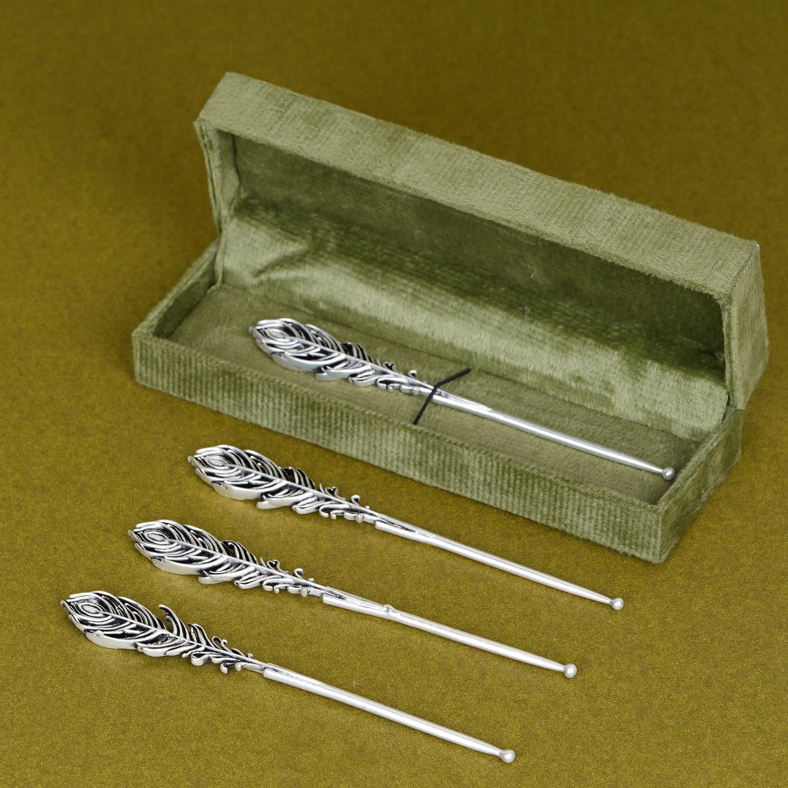 Silver peacock feather tilak sticks with green velvet box on mustard background, Sabera